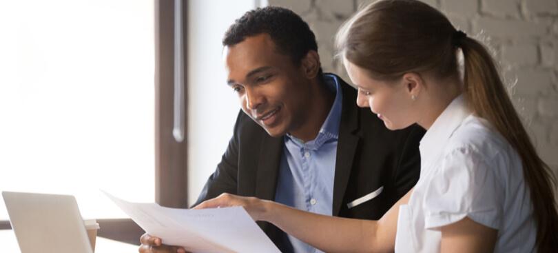 Man holding some documents while a woman points and explains in an office environment