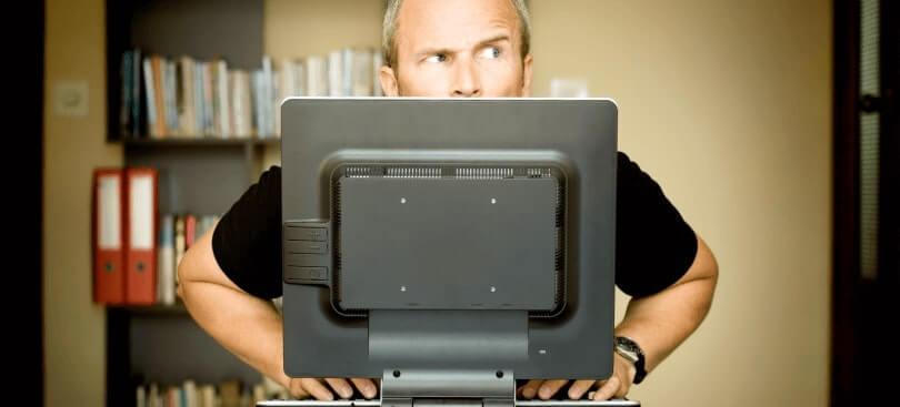 Man looking suspicious behind computer monitor