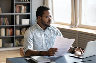 man sitting at table with laptop and papers