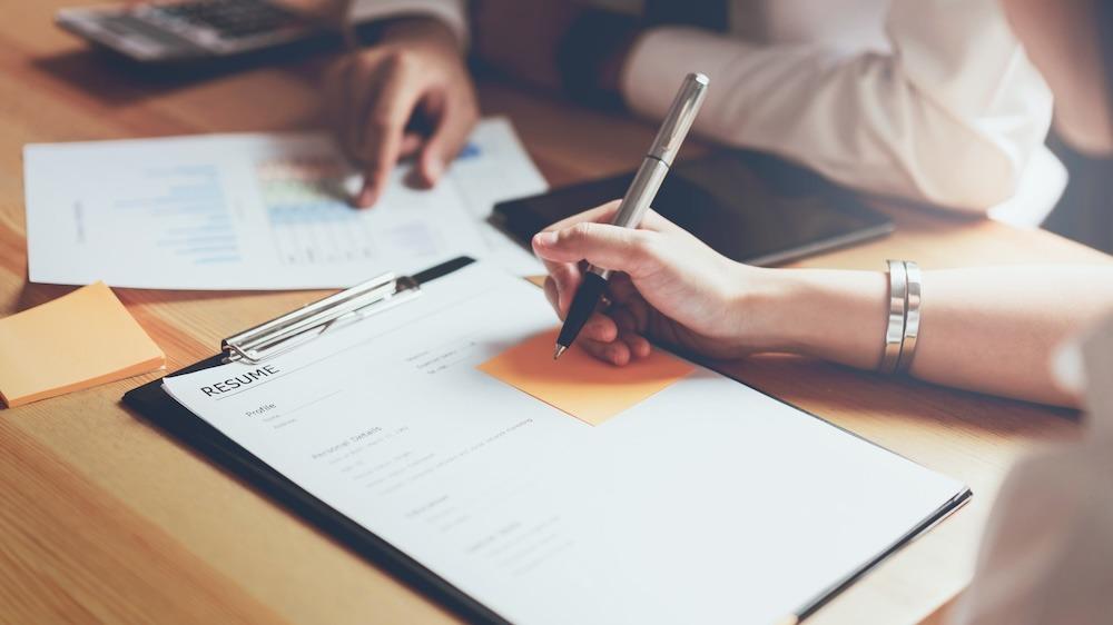 Female hand filling out a resume at a desk for a job application.